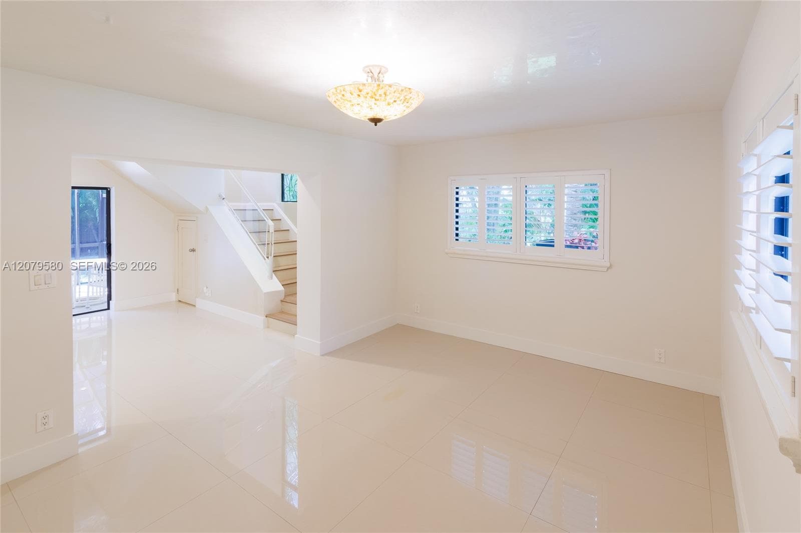 Open interior featuring large-format tile flooring, polished white walls, interior plantation shutters, and an ornate semi-flush mount ceiling fixture