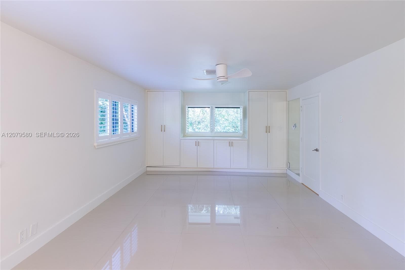 Polished stone flooring, custom built-in cabinetry with metallic pulls, white plantation shutters, and a ceiling-mounted fan