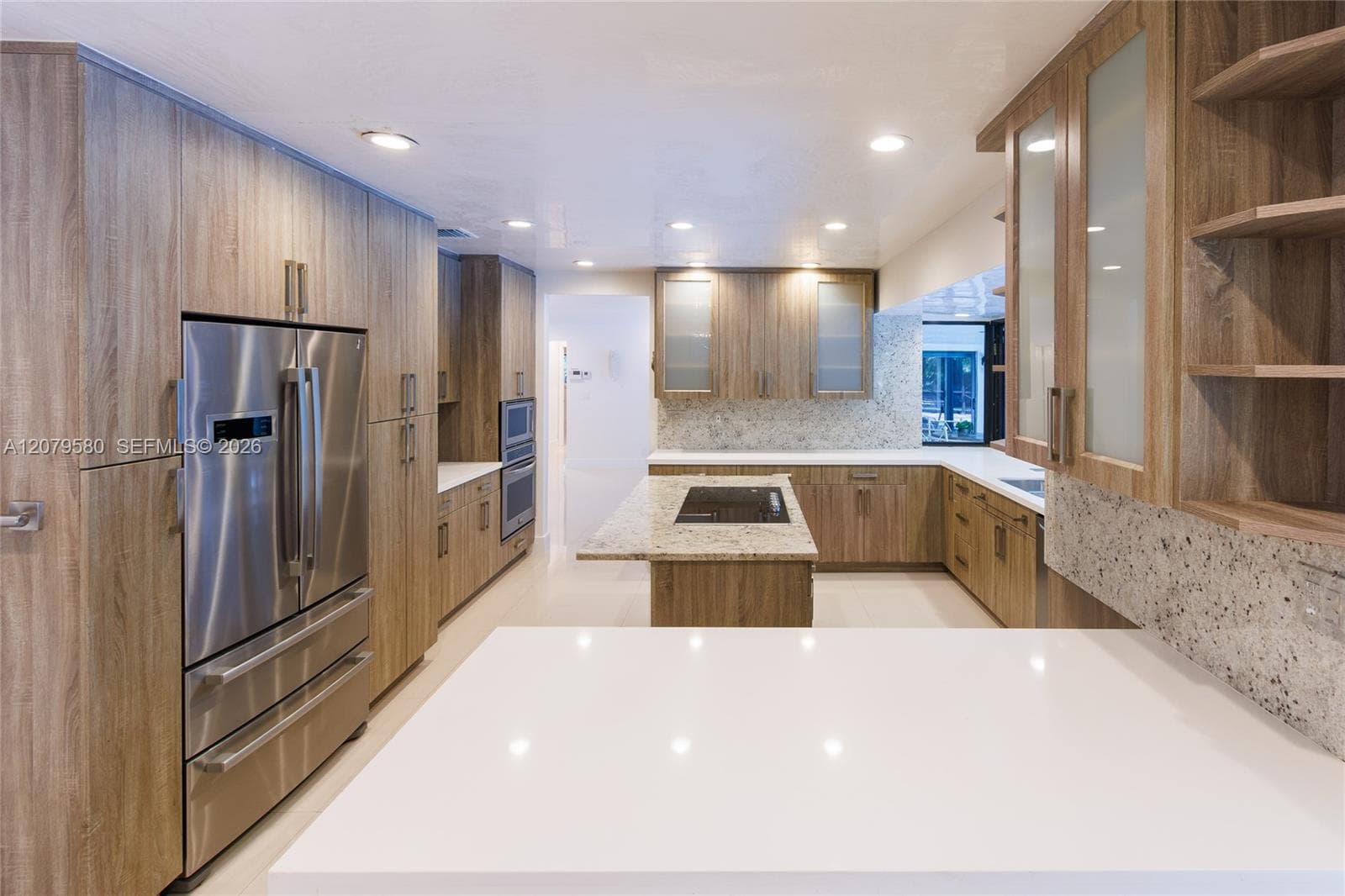 Kitchen featuring wood-finish cabinetry, central island with integrated cooktop, stone-finish countertops, stainless steel appliances, and glass-front upper cabinets