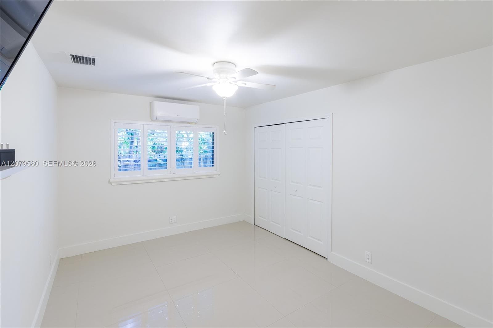 Neutral-toned tile flooring featuring large-format tiles, dual-panel closet doors, wall-mounted ductless climate control system, and window shutters