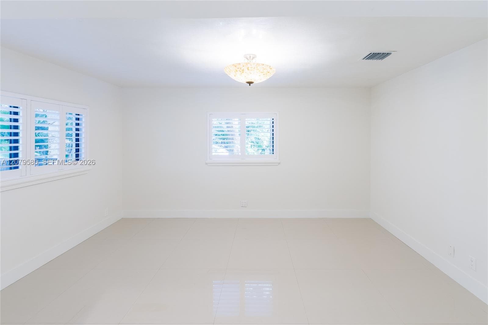 Neutral-toned tile flooring featuring large-format tiles, bright white walls, and white plantation shutters on dual-aspect windows, finished with a central semi-flush mount light fixture