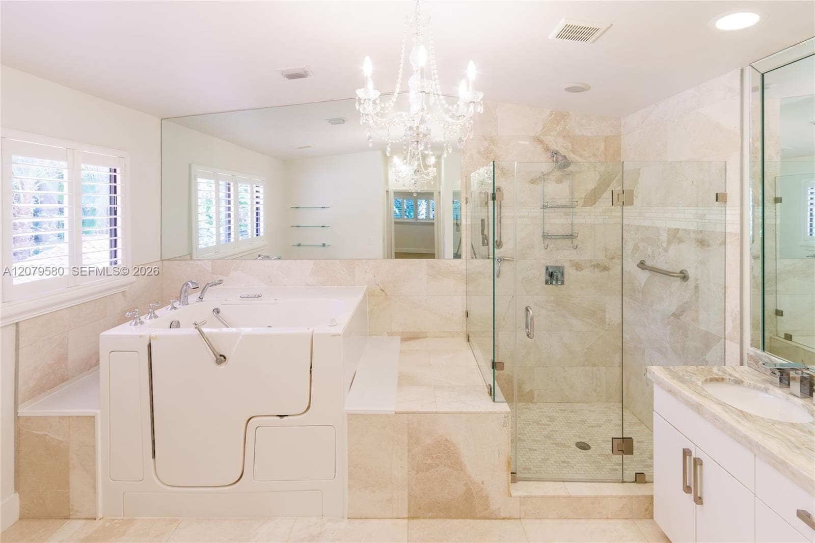 Bathroom featuring a walk-in tub, a frameless glass-enclosed shower with tiled walls, a crystal chandelier, and a vanity with a stone-top surface