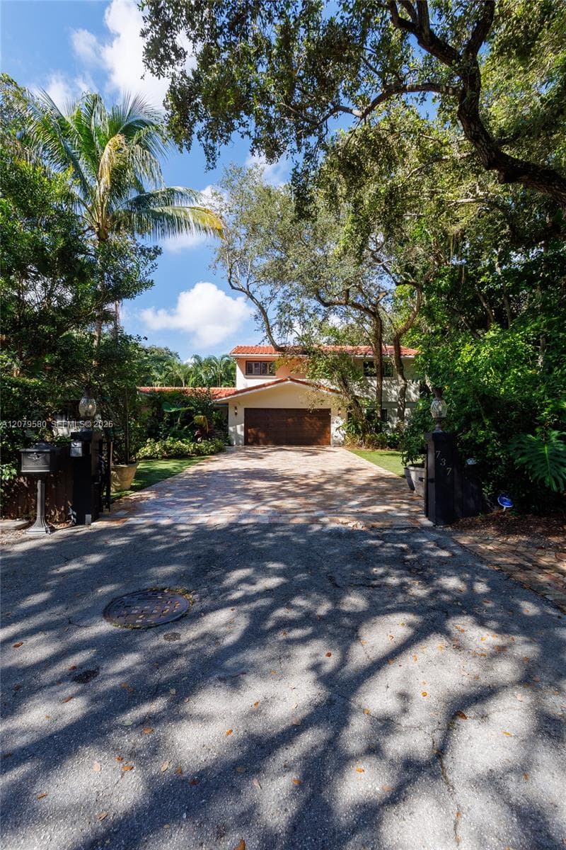 Two-story residence featuring a tile roof, multi-car garage, stone-paved driveway, and mature landscaping