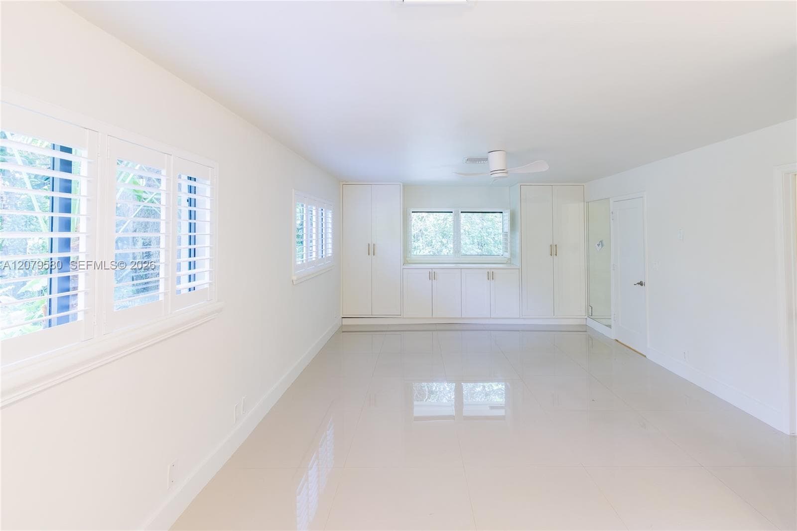 Bright interior featuring white tile flooring, white plantation shutters, built-in cabinetry, and a ceiling fan