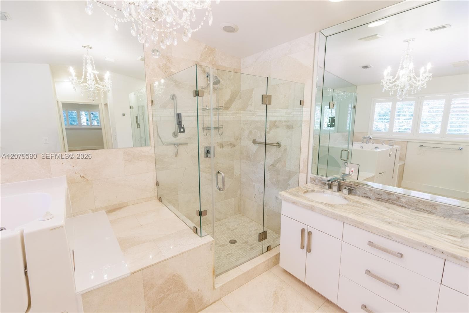 Bathroom featuring a stone-tiled walk-in shower with a glass enclosure, white cabinetry with stone countertops, a dual-basin vanity, and decorative crystal-style chandeliers