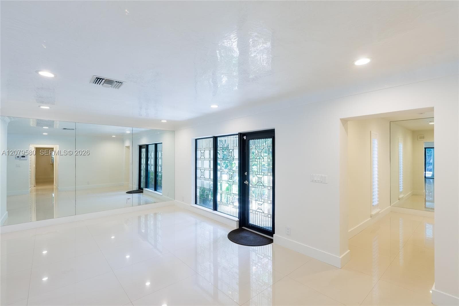Glossy tile flooring, recessed ceiling lighting, wall-to-wall mirrored panels, and a decorative glass-panel entry door