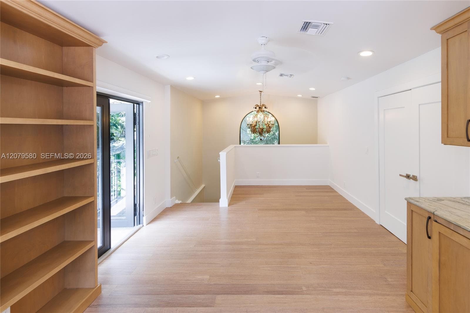 Custom built-in wood shelving, wood-finish flooring, arched window, recessed lighting, and chandelier fixture