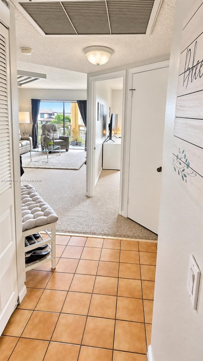 Entryway featuring ceramic tile flooring, neutral carpeting, flush-mount ceiling lighting, and louvered closet doors