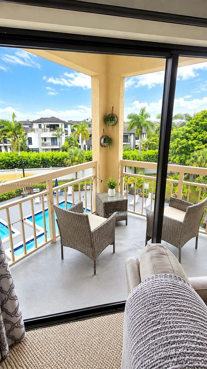 Covered balcony with structural railing and concrete flooring, overlooking a swimming pool and landscaped grounds