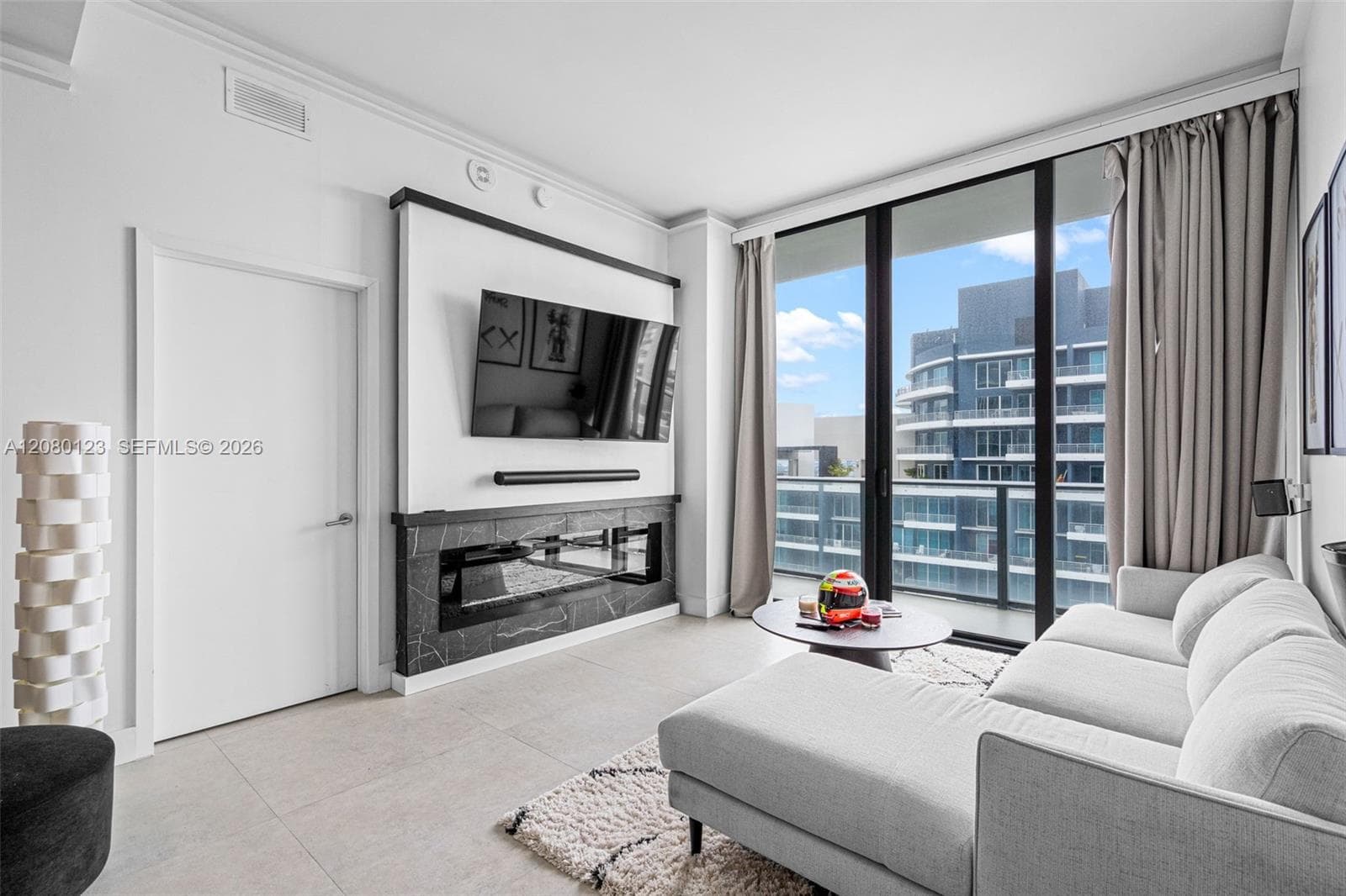 Penthouse living room with mounted TV, modern furnishings, and floor-to-ceiling glass opening to panoramic Brickell views.