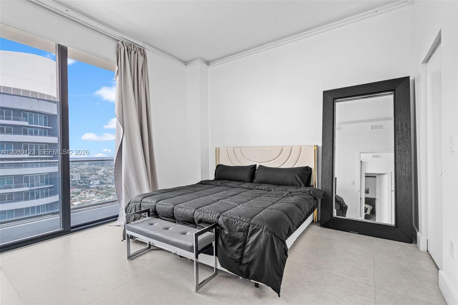 Bright king-size primary bedroom with floor-to-ceiling glass, designer mirror, and tranquil skyline outlook from the 52nd floor.
