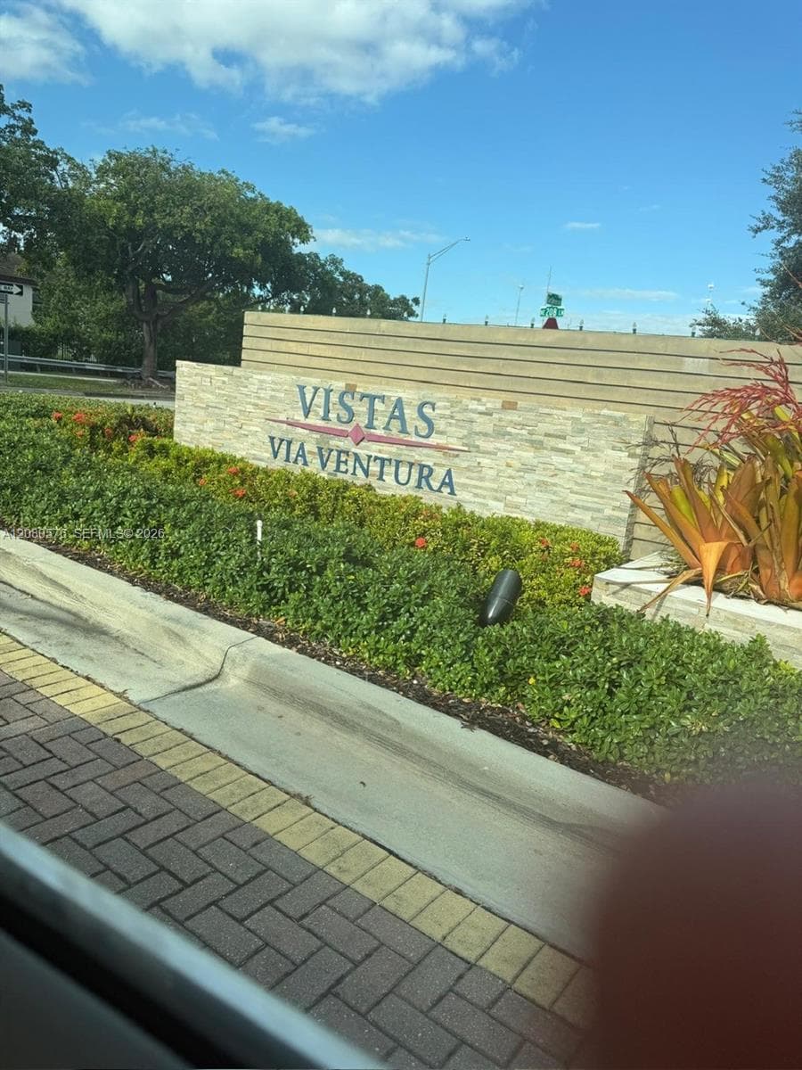 Community entrance featuring a stacked-stone monument sign, horizontal slat fencing, paved brick walkway, and manicured landscaping with integrated low-voltage lighting