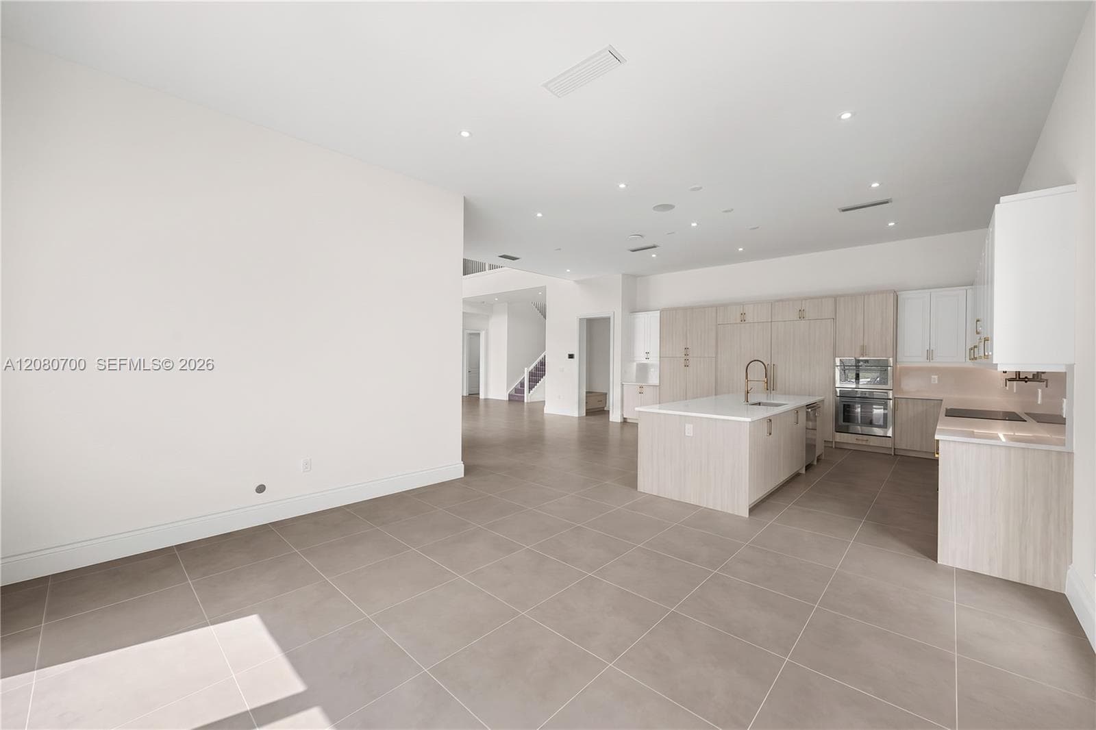 Spacious open-concept area featuring a gourmet kitchen with a central island, integrated appliances, recessed lighting, and large format tile flooring