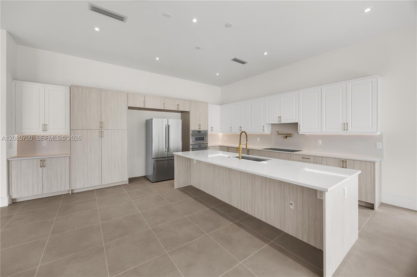 Spacious kitchen featuring an expansive island, stainless steel appliances, integrated cooktop, abundant cabinetry, and tile flooring