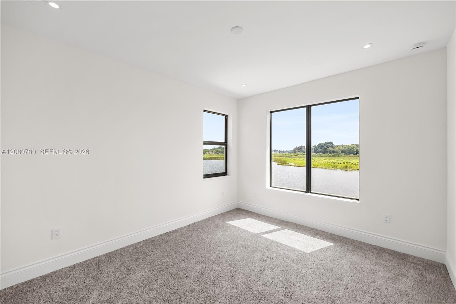 Recessed lighting illuminates this room, featuring two black-framed windows and gray carpeting