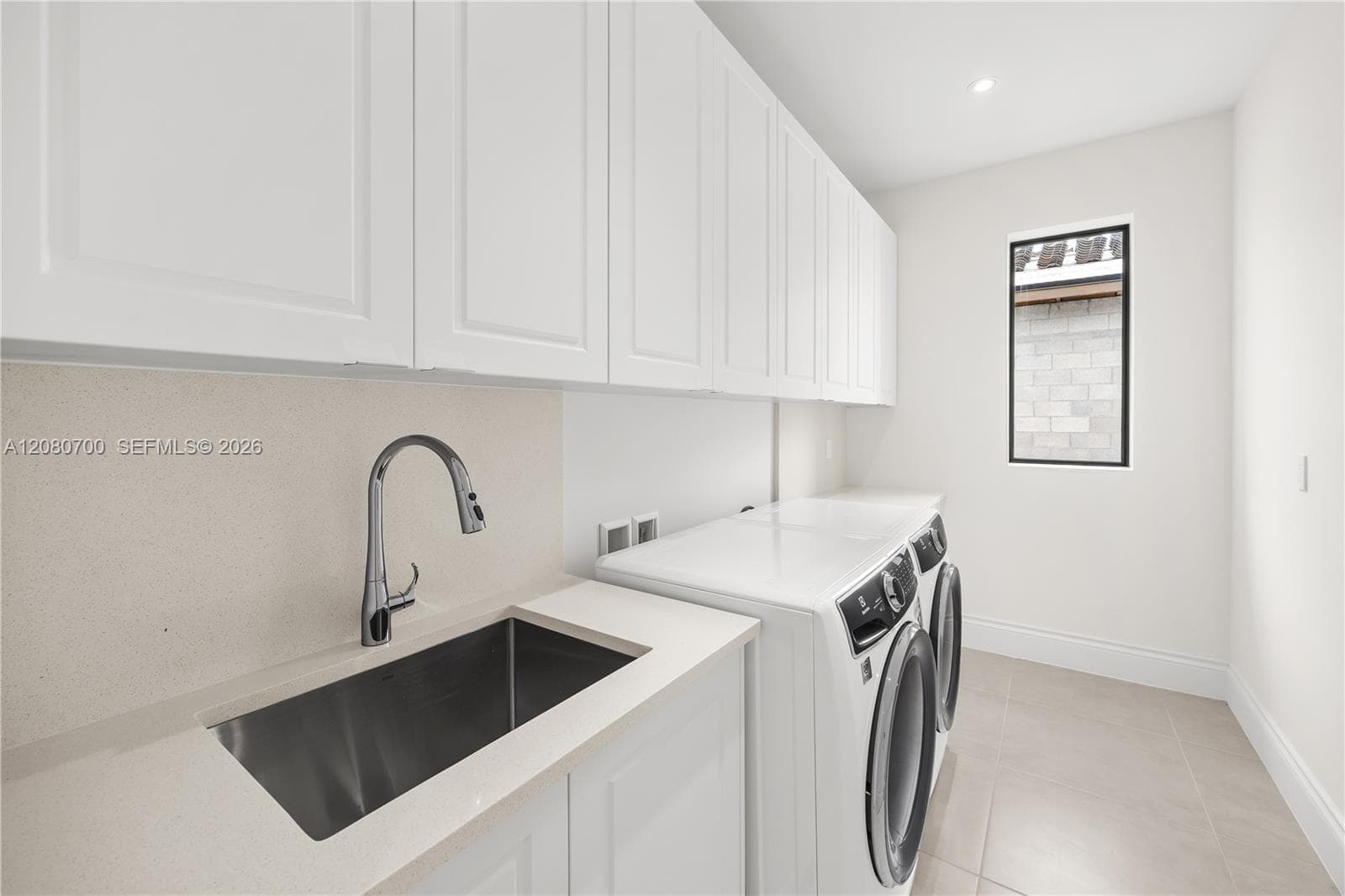 White shaker-style cabinetry, a stainless steel sink with a chrome gooseneck faucet, light-toned countertops, and tile flooring