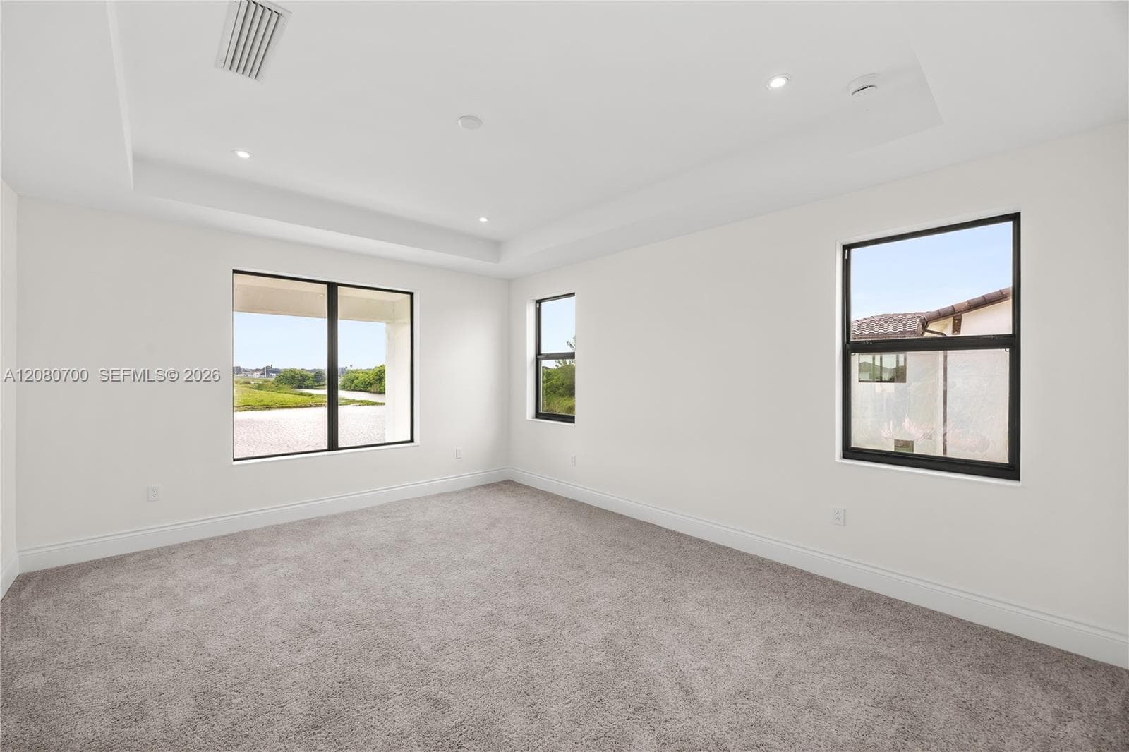 Tray ceiling with recessed lighting, wall-to-wall carpeting, multiple large windows, and clean white walls