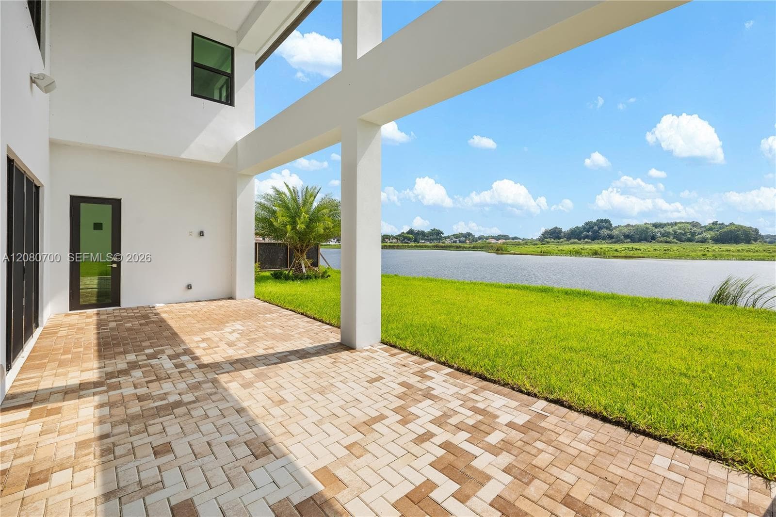 Covered patio with paver flooring, extensive lawn, and waterfront access