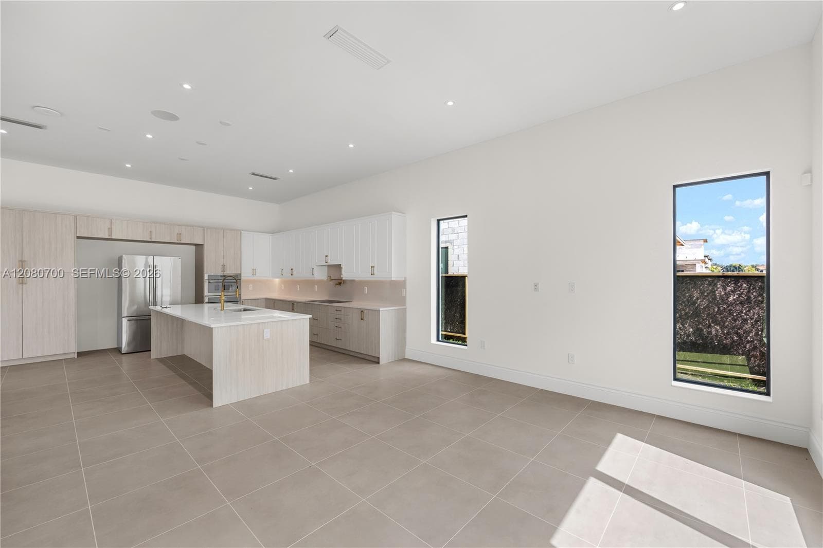 Expansive open-concept space featuring large format floor tiling, a kitchen island with a built-in sink, recessed lighting, and rectangular windows