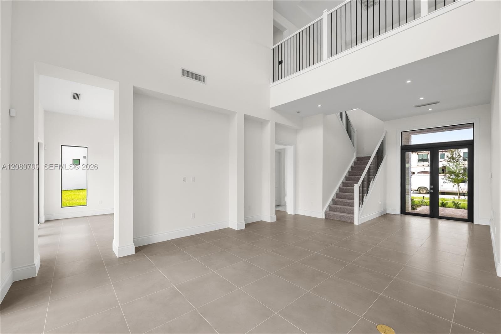 Two-story foyer with high ceilings, large format tile flooring, a modern staircase with metal balusters, and a glass-paneled entry door