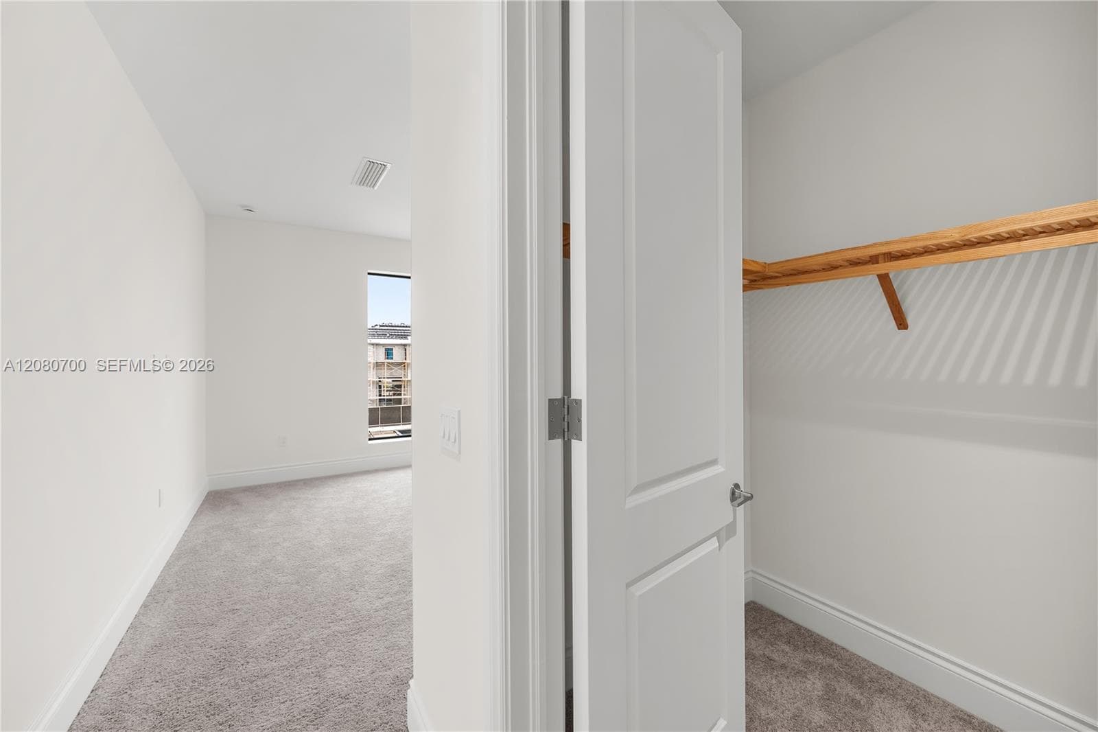 White interior walls, light gray carpeting, and a built-in closet with wood shelving