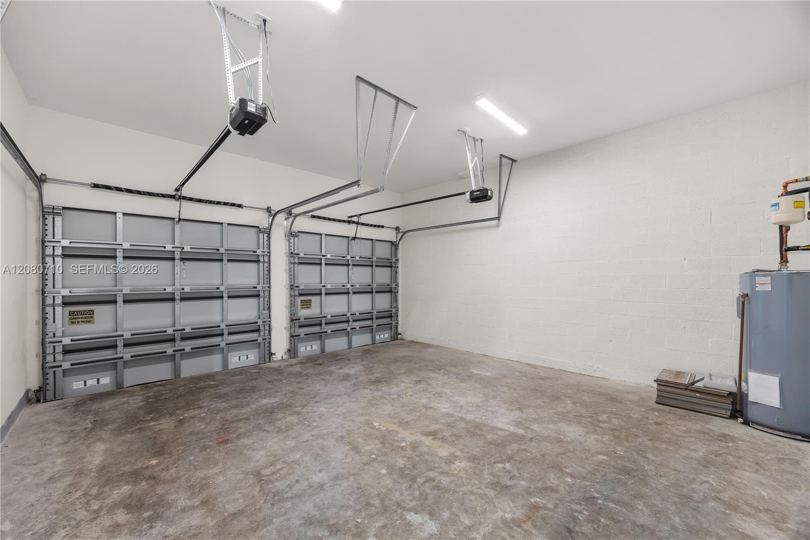 Two garage doors with automatic openers, concrete floor, and fluorescent lighting