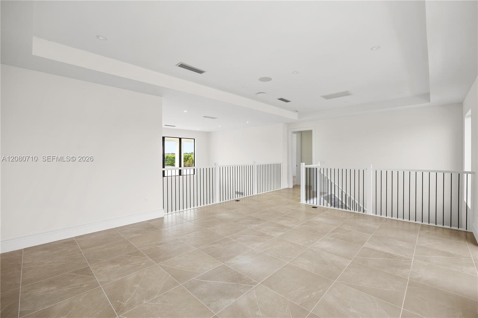 Spacious upper-level area with large format tile flooring, contemporary white railings with vertical balusters, and a tray ceiling