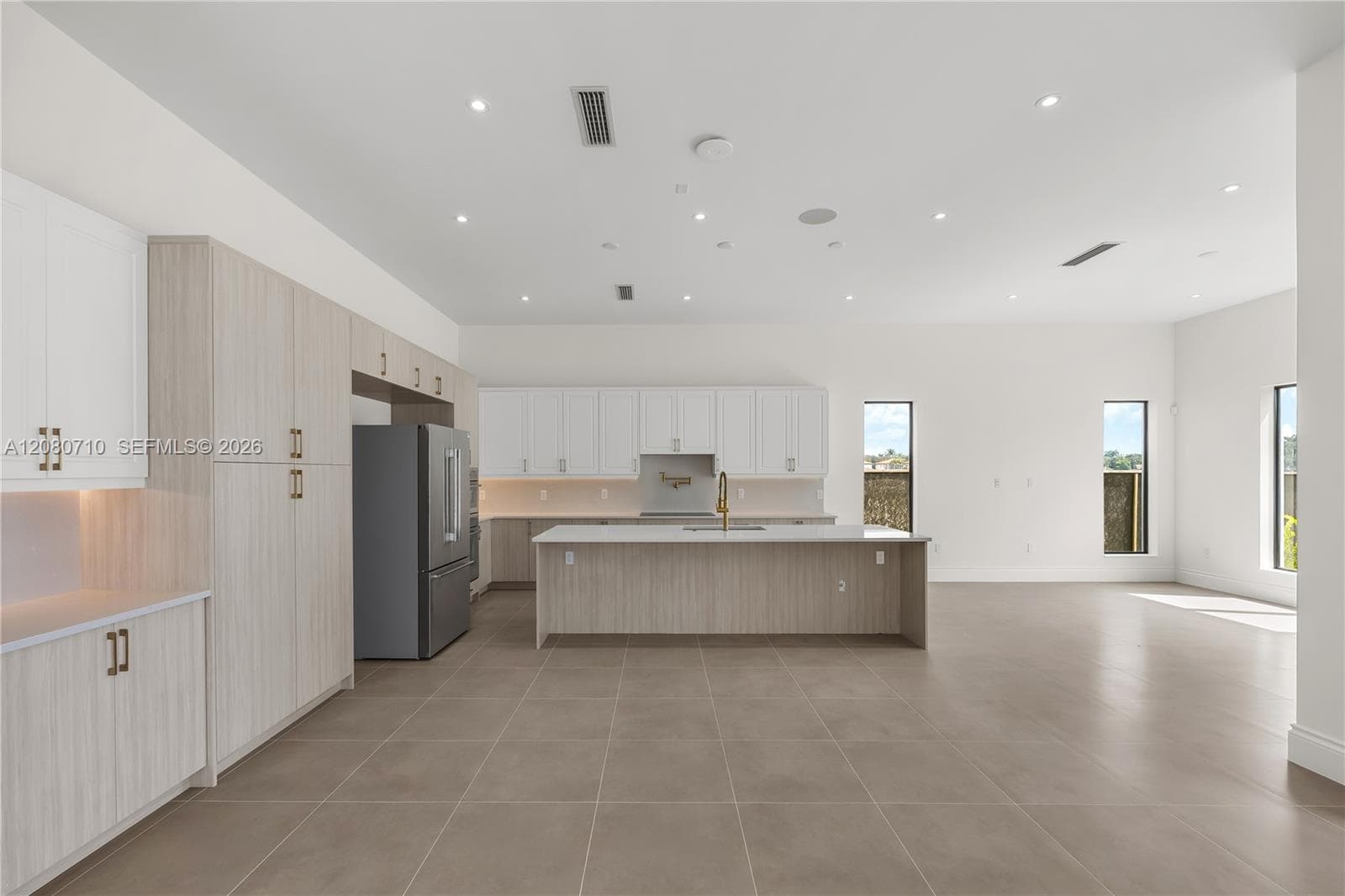 Kitchen featuring a central island with a solid surface countertop, two-toned cabinetry, stainless steel refrigerator, recessed lighting, and tile flooring