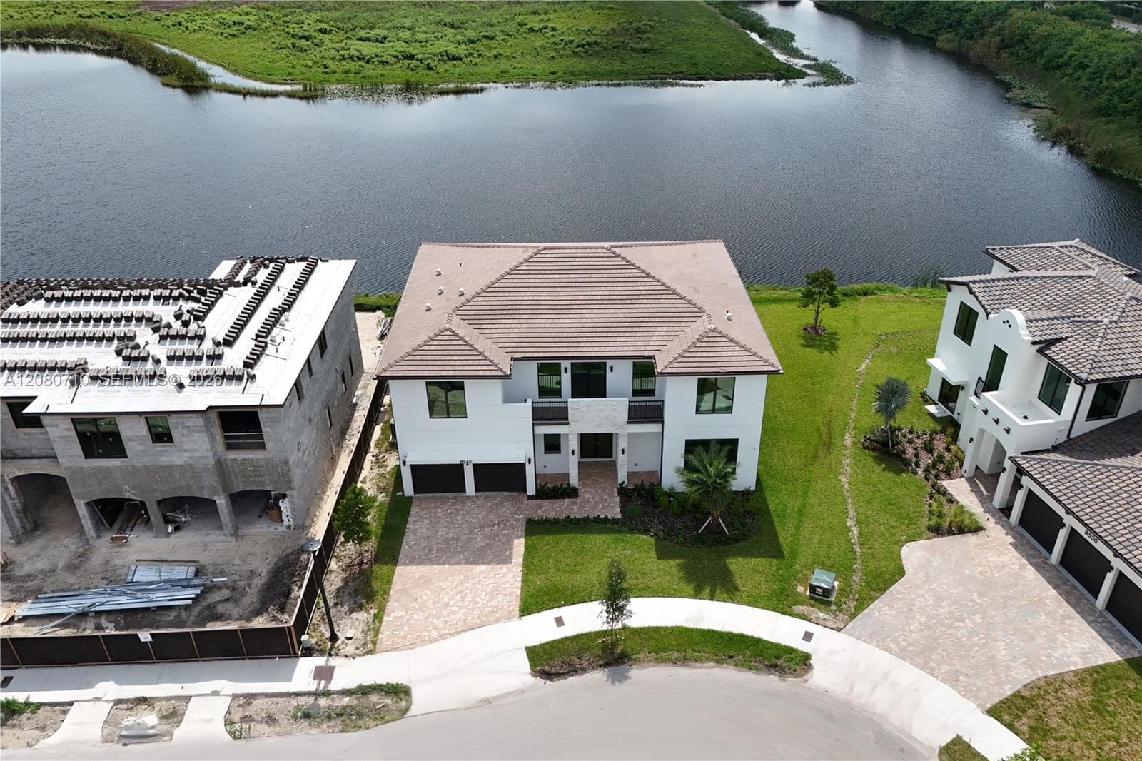 White exterior with contrasting dark window frames, tiled roof, attached two-car garage, and a paver driveway