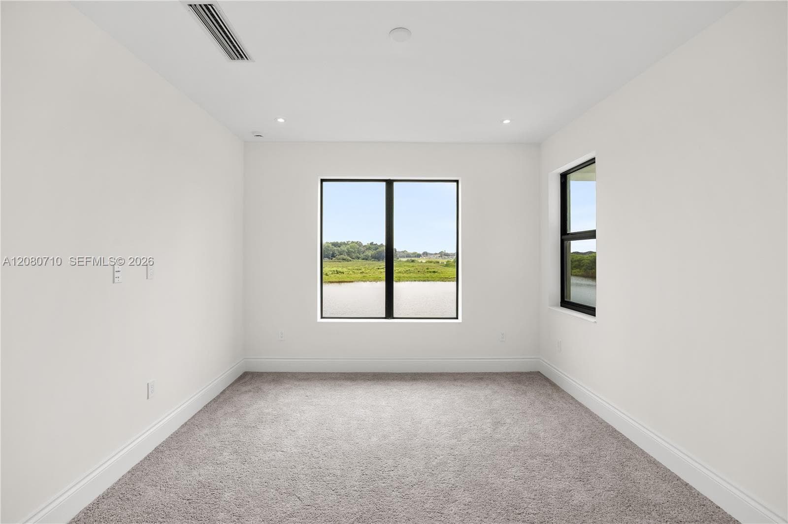 Recessed lighting, large windows with black frames, white walls, and gray carpeting
