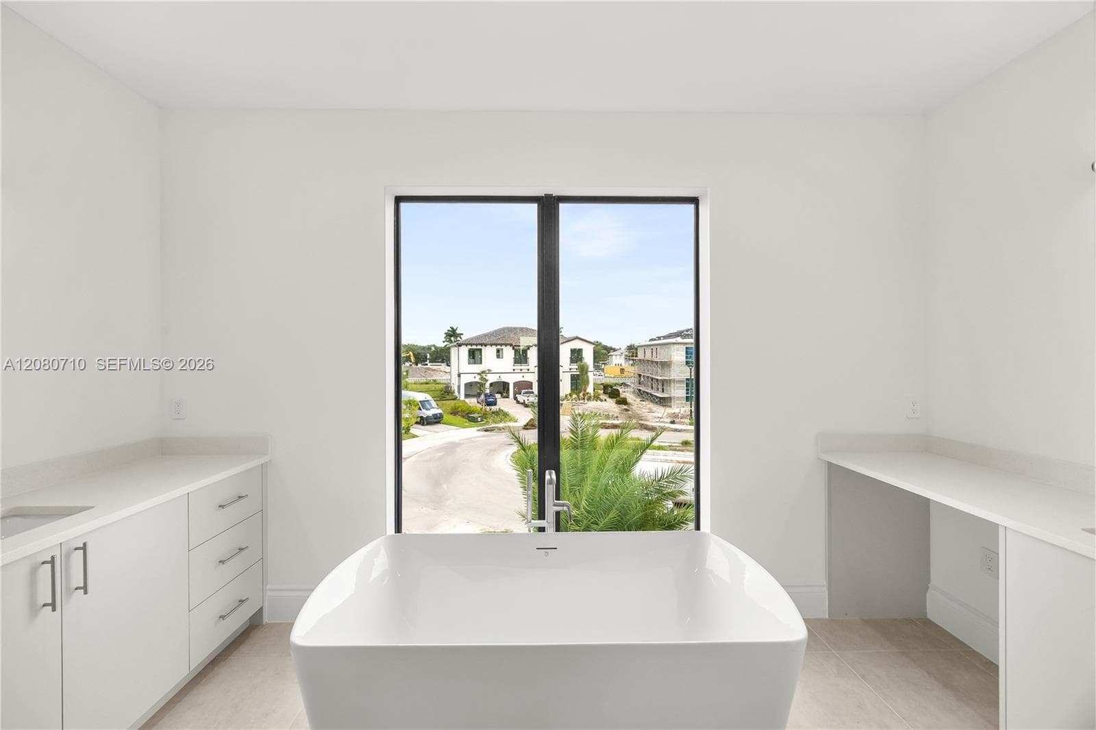 Freestanding soaking tub with polished chrome faucet, flanked by custom white cabinetry featuring white countertops and clean-lined hardware, set before a large black-framed picture window