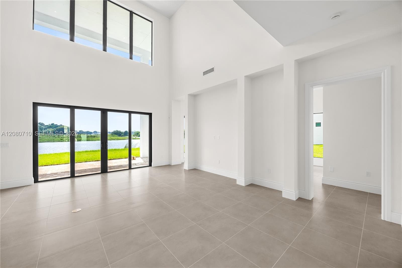 Soaring ceilings with transom windows, large format tile flooring, and a sliding glass door with a water feature backdrop