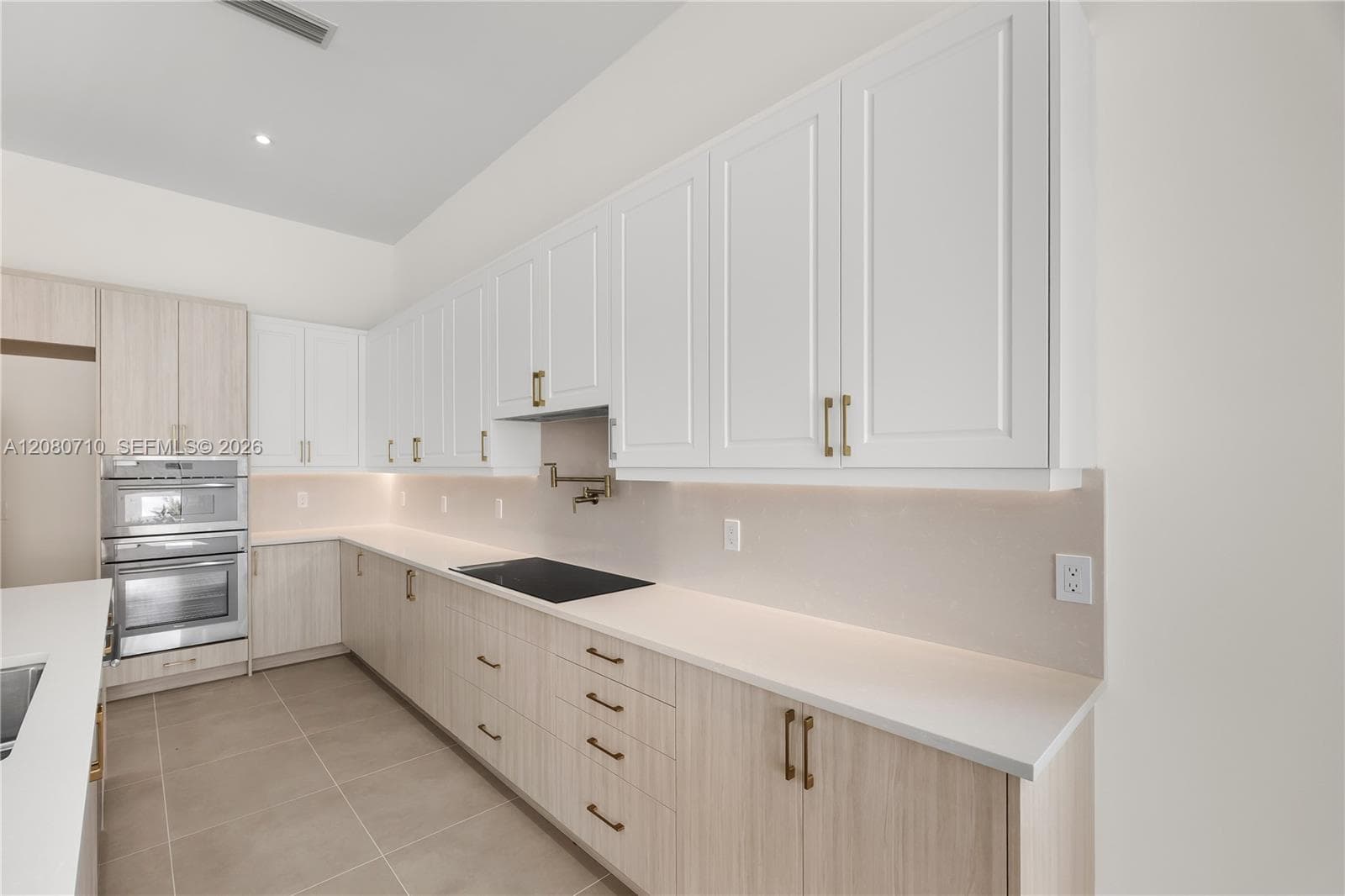 Kitchen featuring light wood-finish cabinetry, white shaker-style upper cabinets, solid-surface countertops, a recessed cooktop, and an articulated pot filler faucet