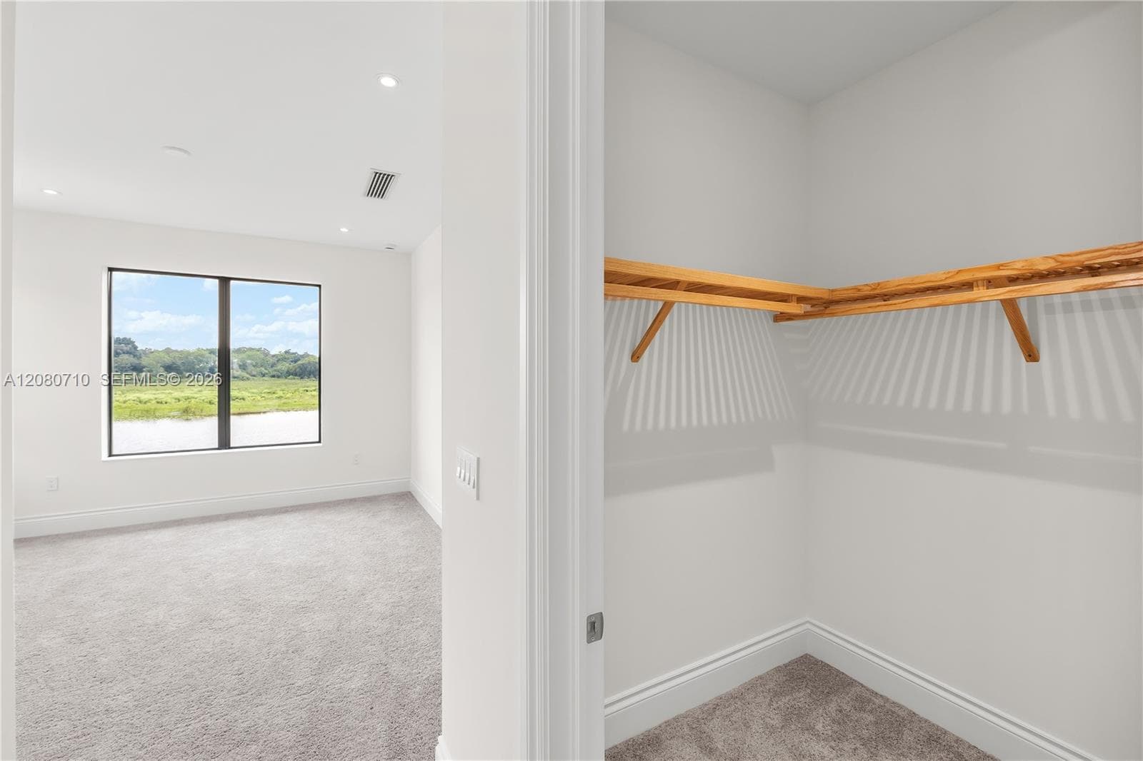 Recessed lighting, large window with expansive outdoor scenery, light gray carpeting, and a built-in closet with wood shelving