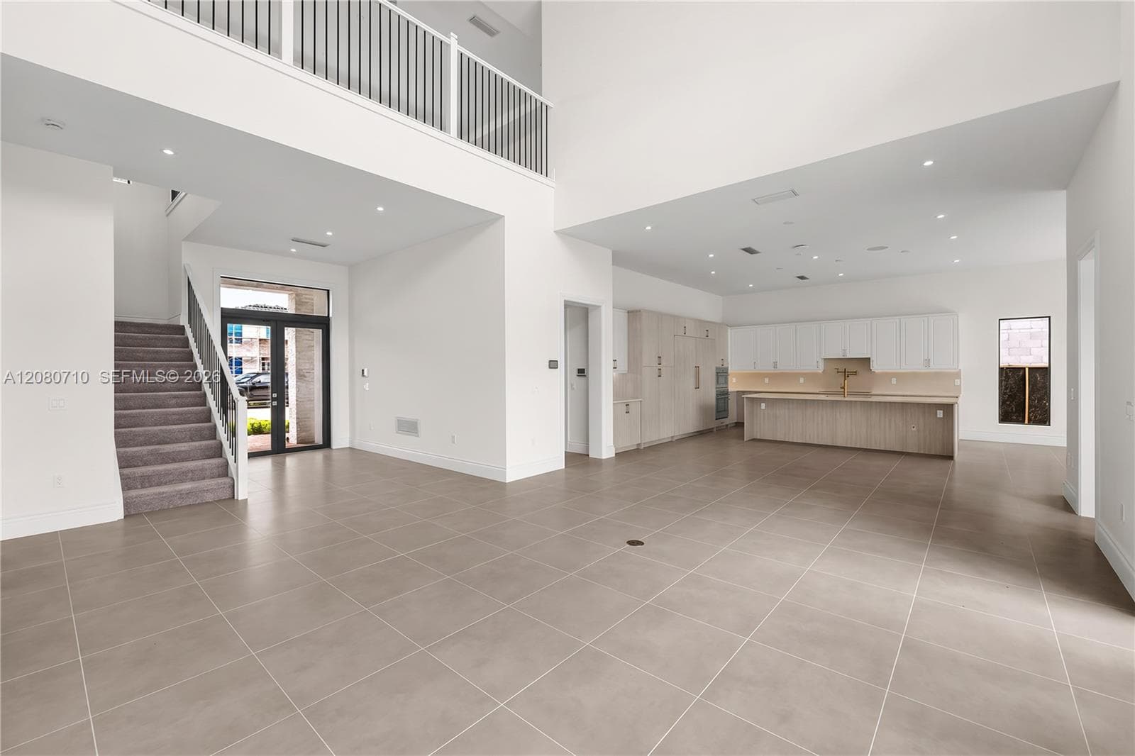 Spacious interior featuring large format tile flooring, a contemporary kitchen with light wood-finish cabinetry, a second-story landing with an iron railing, and a carpeted staircase
