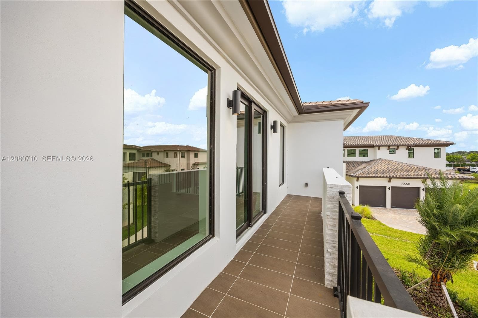 Exterior balcony featuring modern black railings, brown tile flooring, and sliding glass doors