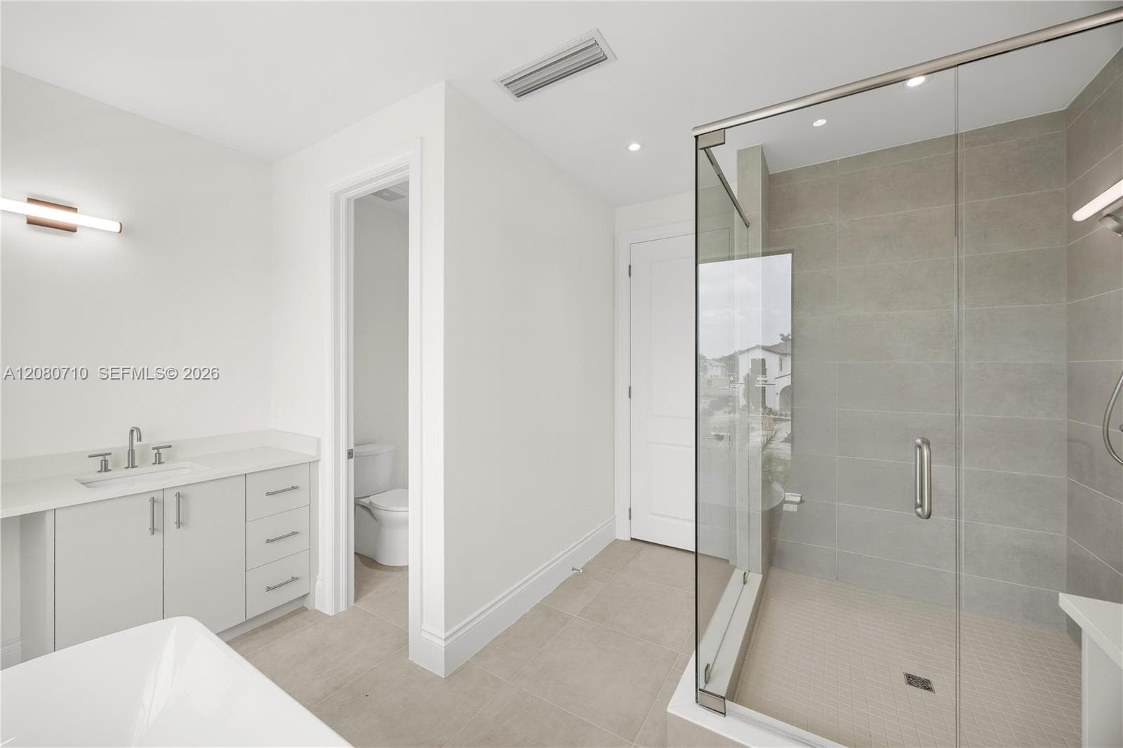 Walk-in shower with clear glass enclosure and light-toned tile surround, single vanity with light cabinetry and solid surface countertop, and tile flooring