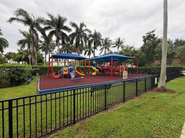 Fenced playground featuring multiple play structures, a slide, and a seesaw