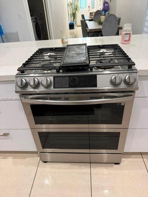 Stainless steel range with a built-in griddle and double ovens, set into a light-toned countertop, complemented by white cabinetry and tile flooring