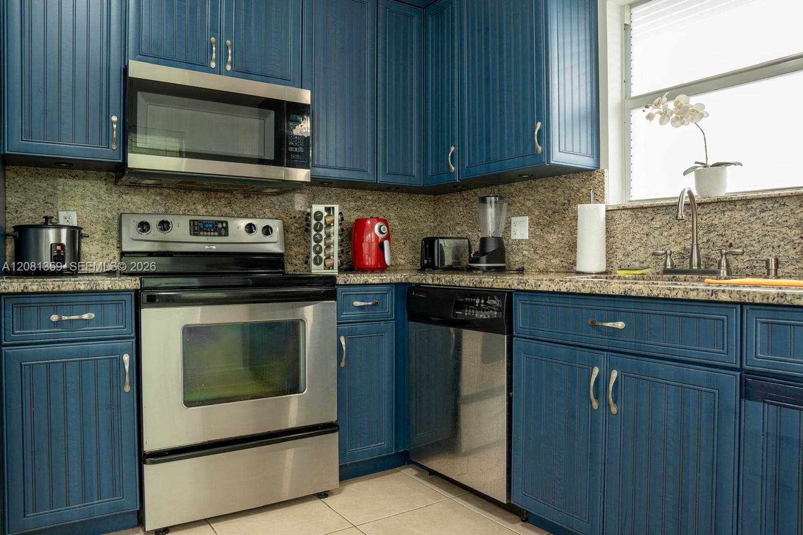 Kitchen featuring beadboard-style cabinetry, stone countertops, stainless steel appliances, and a double-basin undermount sink