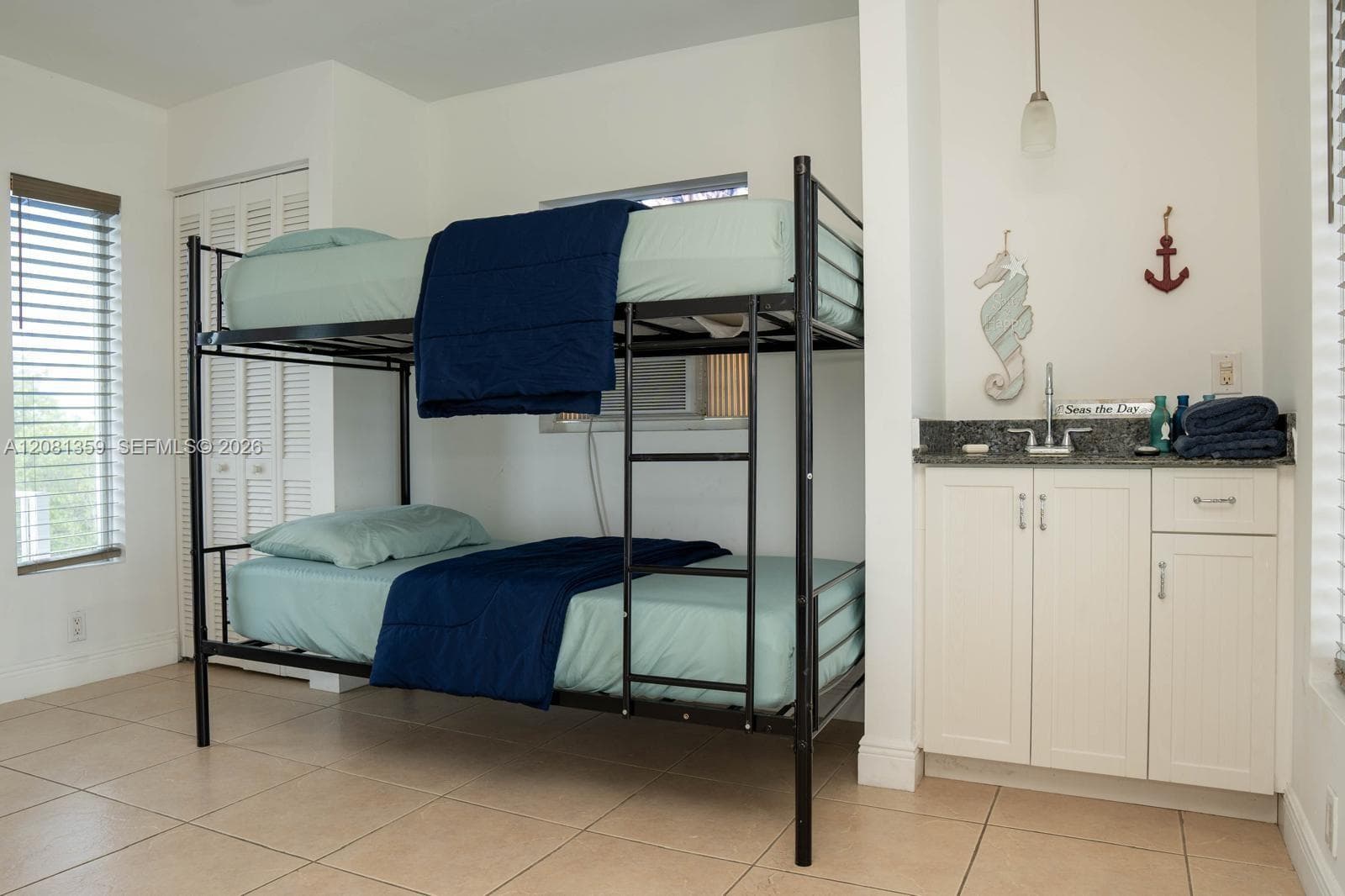Bright bedroom featuring a full-size metal bunk bed frame with dual sleeping stations, neutral tile flooring, and ample natural light from shuttered windows