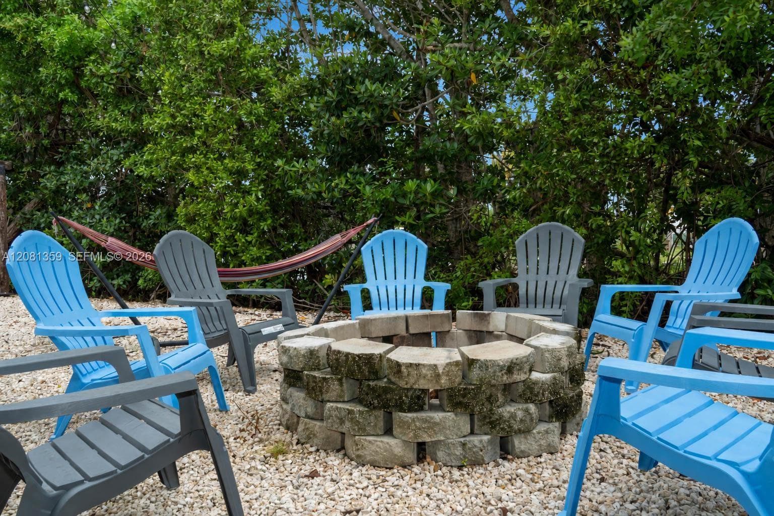 Circular stone fire pit featuring dry-stacked masonry construction situated on a gravel surface with mature perimeter landscaping