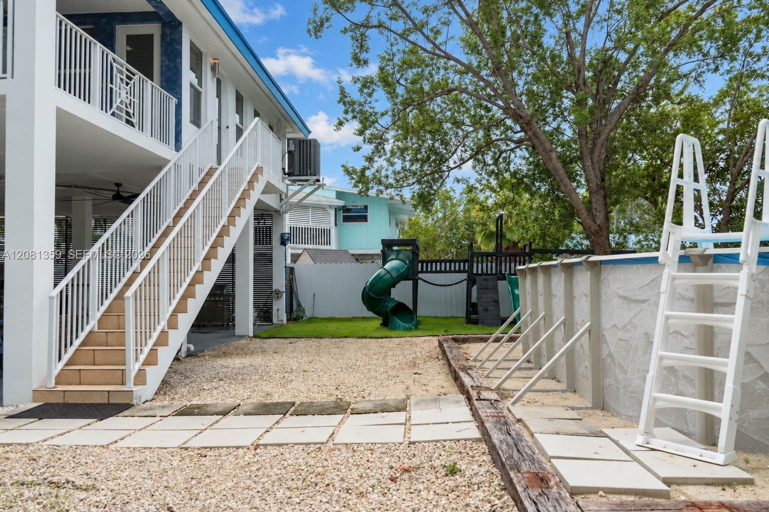 Outdoor space featuring a raised exterior staircase with white metal railings, an above-ground pool, stone paver pathways, and a privacy fence