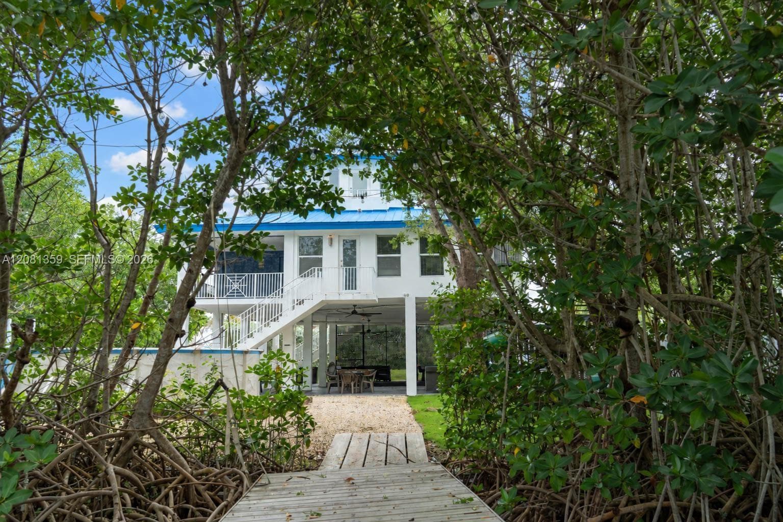 Stilt-constructed residence featuring a metal roof, screened-in porch, exterior staircase, and a ground-level covered patio, accessed by a private wooden dock