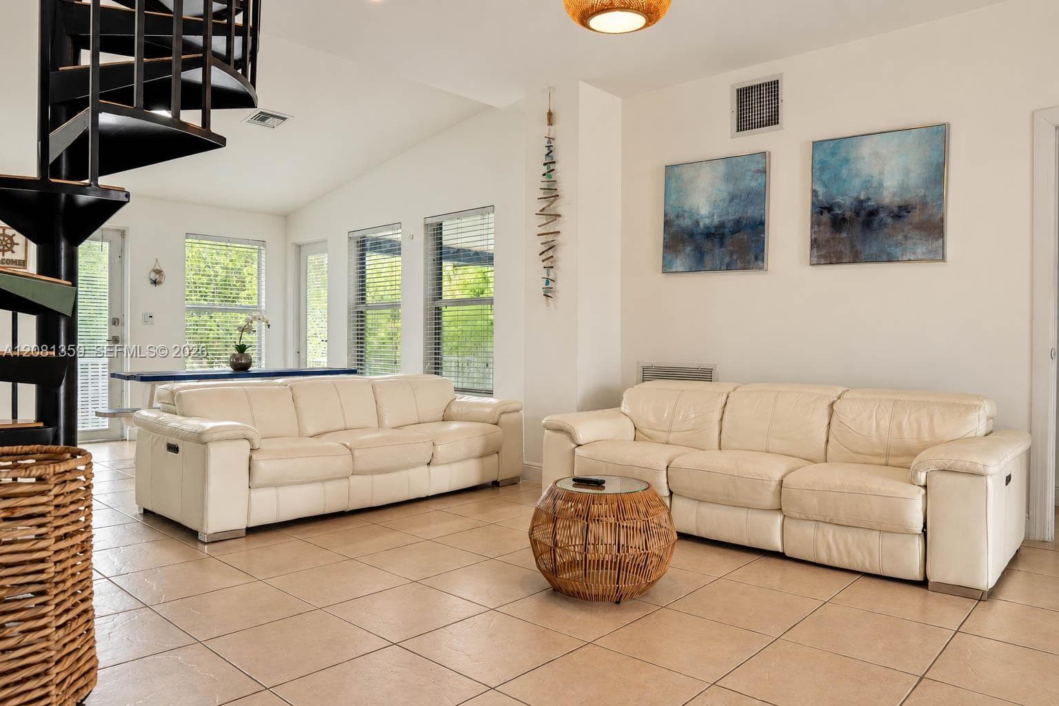 Living area featuring a black metal spiral staircase, vaulted ceiling, large windows with horizontal blinds, and tile flooring