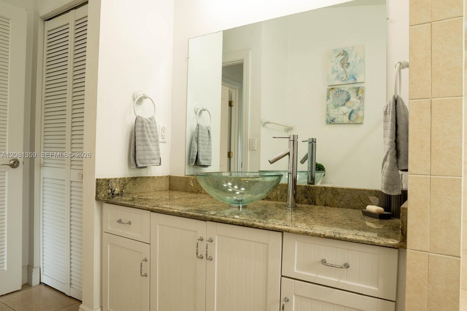 Bathroom vanity featuring white cabinetry, stone countertop, glass vessel sink, high-arc faucet, and a large wall-mounted mirror