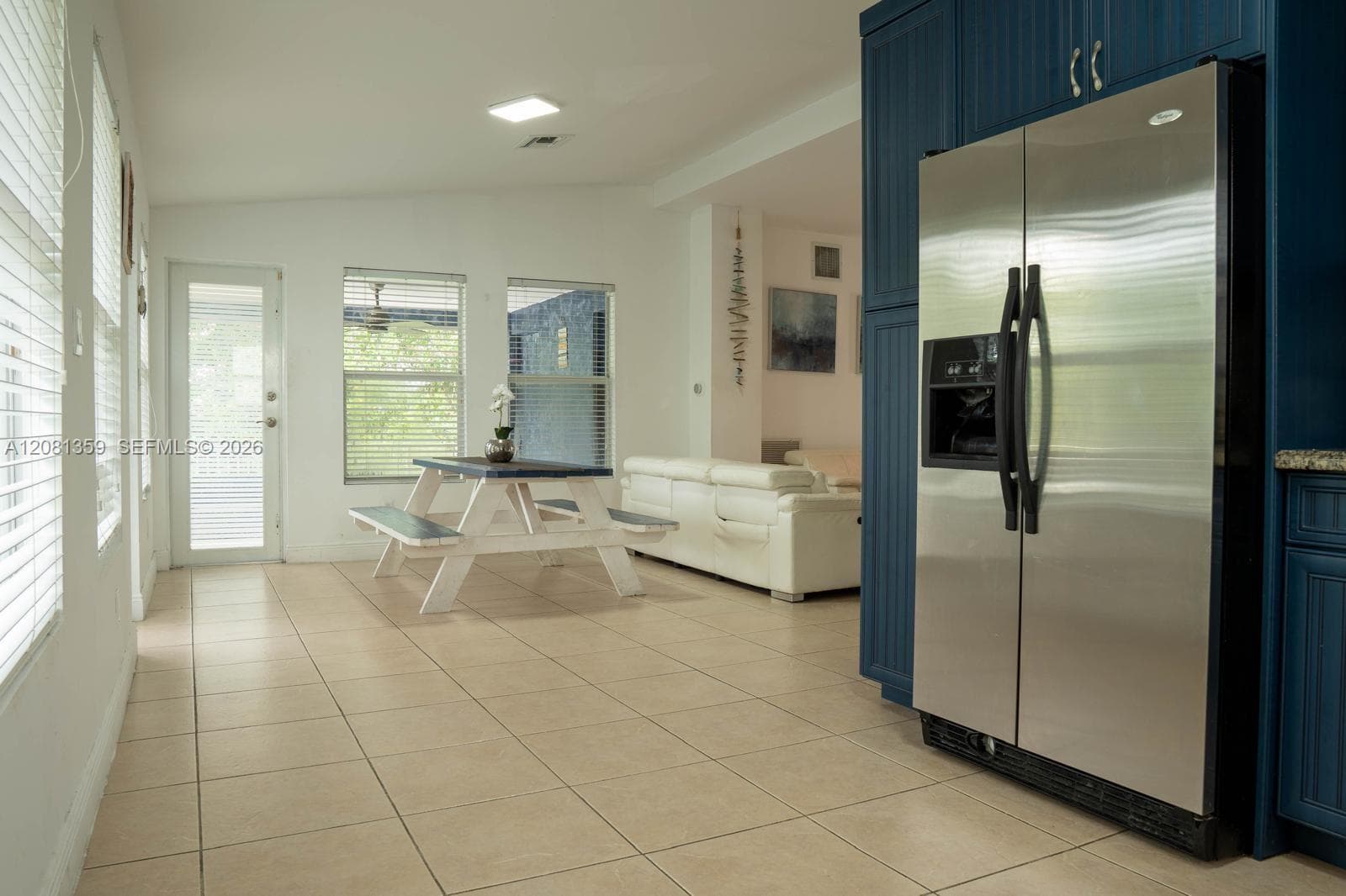 Kitchen featuring blue cabinetry, stainless steel side-by-side refrigerator, tile flooring, and windows with integrated blinds