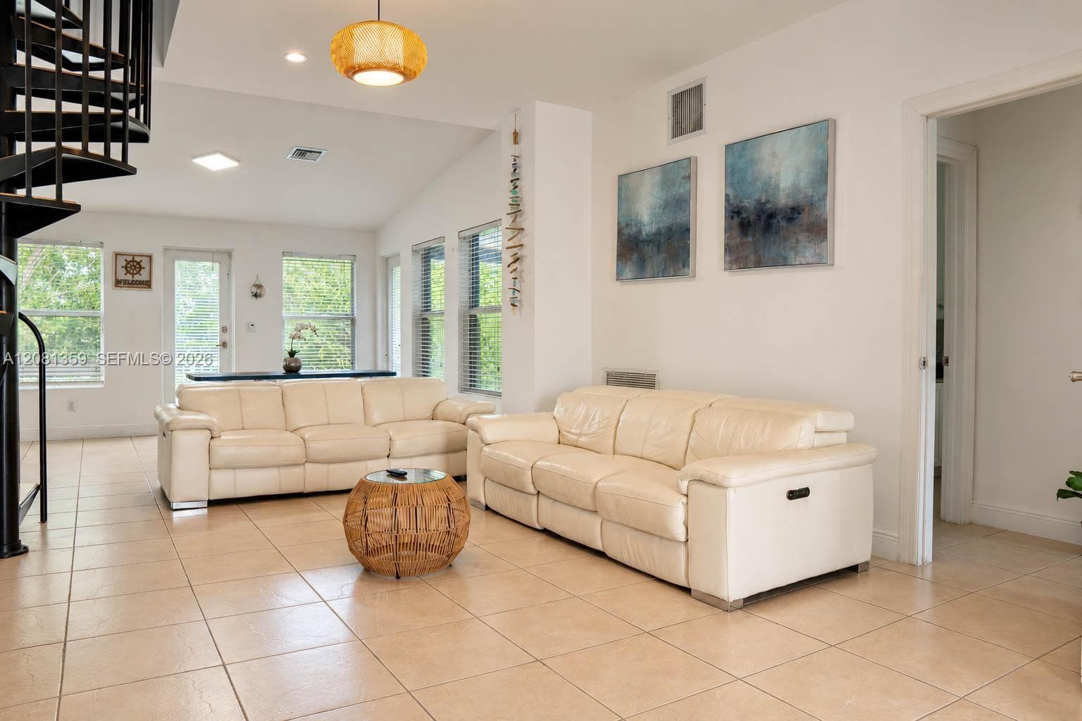 Open-concept interior featuring large-format tile flooring, a black metal spiral staircase, vaulted ceilings, and multi-pane windows