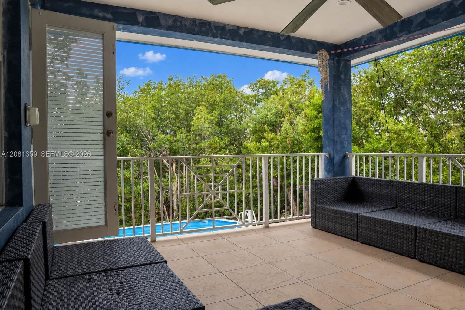 Covered balcony featuring tile flooring, a white metal railing, textured blue pillars, and a ceiling-mounted fan