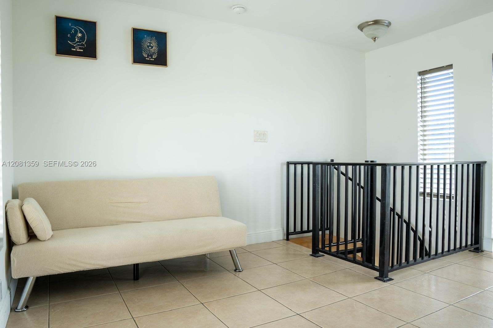 Neutral-toned tile flooring, black metal railing with vertical balusters, and a flush-mount light fixture
